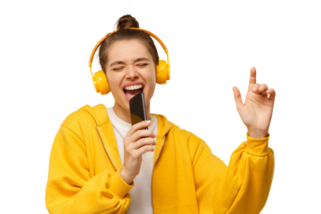 Young girl in yellow hoodie and wireless headphones, singing with closed eyes, holding smartphone as microphone