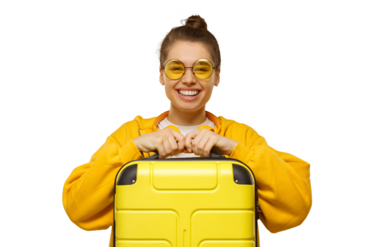 Young smiling woman in yellow hoodie and colored glasses holding travel suitcase, willing to go on trip