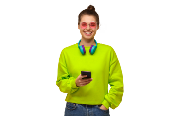 Happy girl wearing green neon top, jeans, pink glasses and wireless headphones around neck, holding phone in hand