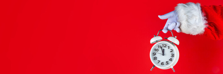 Santa Claus hand holding white alarm clock on red background