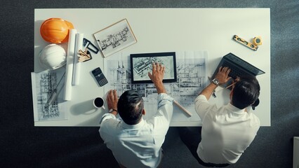 Top view of skilled civil engineer working together to plan building design. Top down aerial view of skilled architect team sitting at table while manager using tablet open project plan. Alimentation.