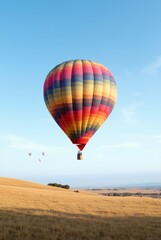 Naklejka premium Colorful Hot Air Balloon Ascending Over Golden Fields at Sunrise Near a Tranquil Landscape