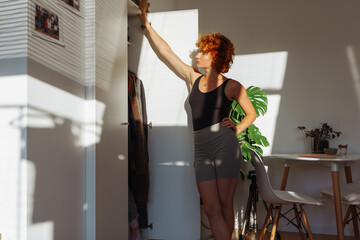 portrait of young red-haired woman choosing clothes in closet at home