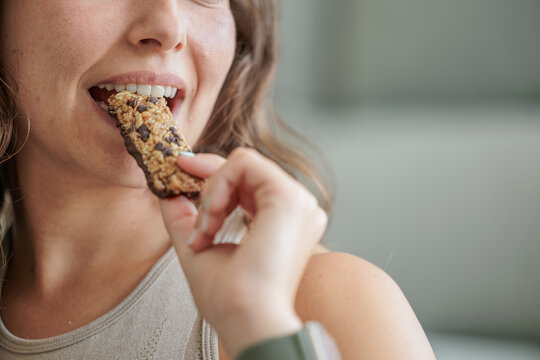 Portrait of a smiling young woman eating a protein bar with chocolate chips. Close up, copy space.