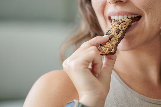 Portrait of a smiling young woman eating a protein bar with chocolate chips. Close up, copy space.
