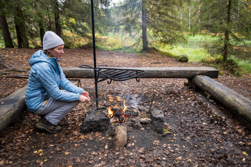 woman in the blue jacket cooking on a campfire in the forest