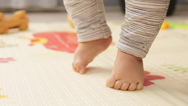Closeup of unrecognizable small baby feet on colorful floor first steps barefoot on carpet suffering fragility and weak muscles