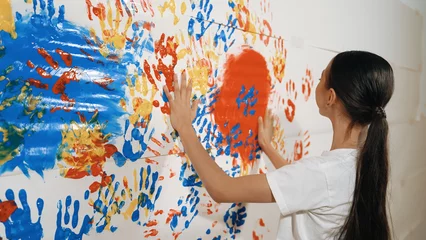 Gardinen Farbenfroh Asian girl use hand to stamp the wall with red color in art lesson. Multicultural highschool student wear white shirt while paint room with colorful hand print. Creative activity concept. Edification.  © InfiniteFlow