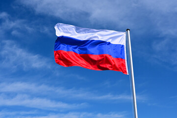 The flag of Russia flutters in the wind against a blue cloudless sky