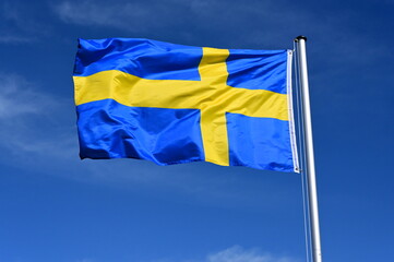 The flag of Sweden flutters in the wind against a blue cloudless sky
