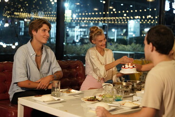 Friends partying on a birthday, blowing out candles on a cake, having fun and having dinner together at a restaurant.