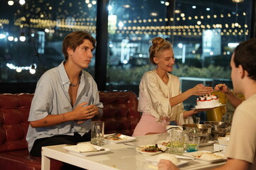Friends partying on a birthday, blowing out candles on a cake, having fun and having dinner together at a restaurant.