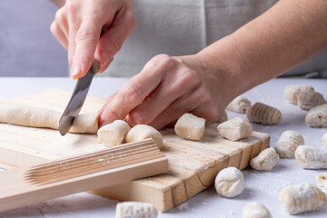 Close-up of human hands cutting a strip of dough to make gnocchi, on a wooden board.
