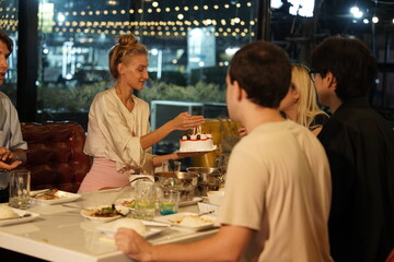 Friends partying on a birthday, blowing out candles on a cake, having fun and having dinner together at a restaurant.