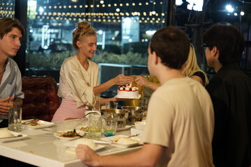 Friends partying on a birthday, blowing out candles on a cake, having fun and having dinner together at a restaurant.