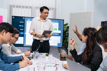 Project manager communicate and collaborate with team using project management software display on monitor, tracking progress of project task and making schedule plan at meeting table. Prudent