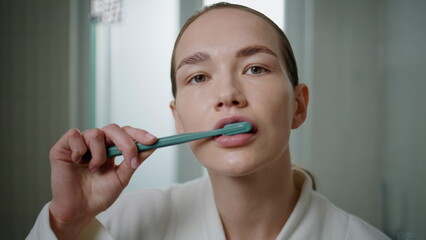 Closeup woman using toothbrush in bathroom setting. Focused girl looking camera