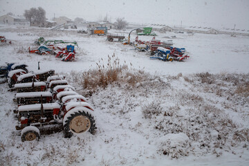 a winter scene on a farm where tractors and various colorful farm machines are covered in a layer...