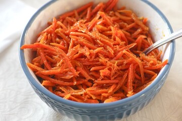 Close-up shot of a blue bowl full of carrot salad with spice and olive oil.