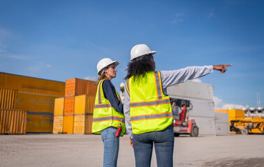 Engineer or dockworker working in the construction container dock yard checking and inspection containers data on computer program environment is container shipping Logistics business concept.