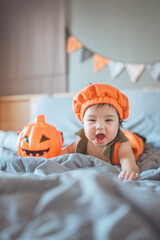 Excited cute asian newborn baby girl dressed in Halloween jack o lantern costume during tummy time...