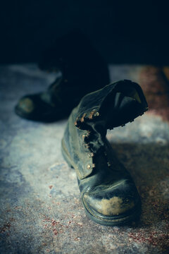 Worn, rugged boots sit on a mottled surface, conveying a sense of history and hardship. The lighting highlights the texture and age of the leather, giving them a nostalgic feel.