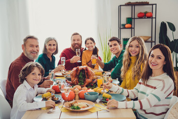 Photo of good mood cheerful people relatives celebrating thanksgiving day sitting eating drinking family gathering indoors