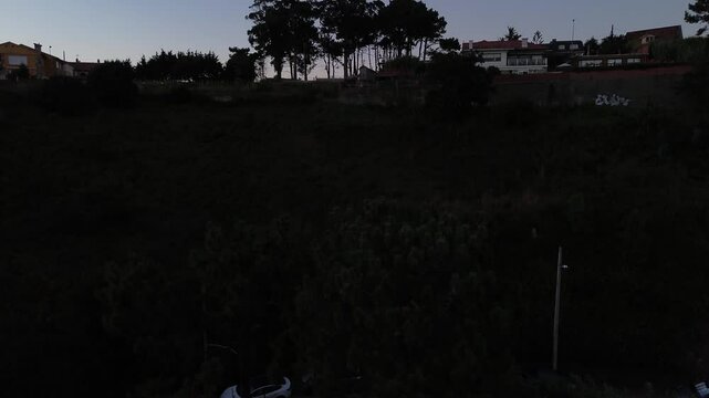 Aerial view of Patos and Prado beaches with houses above, after sunset. Toralla island and Vigo estuary are visible in the distance. View revealed behind Monteferro as camera ascends from Area Fofa.