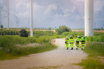 Fototapeta premium A team of engineers in high-visibility safety gear stand together at a wind farm, conducting inspections and discussing renewable energy projects. Wind turbines surround them under a clear sky.