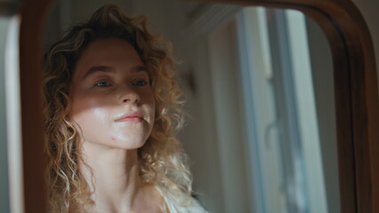Curly woman looking mirror in room sunlight closeup. Thoughtful girl check skin