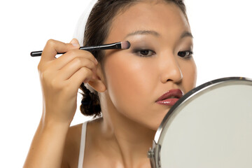 Closeup portrait of a young Asian woman applying eyeshadow.