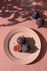 Plate with ripe figs fruit on the mediterranean pink terracotta color plaster background with leaves shadows.