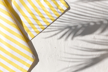 White plaster background with yellow striped pattern napkin or towel with tropical palm leaves shadows. Copy space