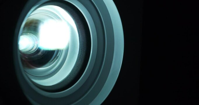 Cinema hall. Close-up of a working projector lens. Movie is shown through projector. Lenses of working projector change color. Light of different colors passes through lenses