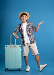 Full body image of Asian guy carrying suitcase travel and posing on blue background