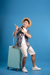 Full body image of Asian guy carrying suitcase travel and posing on blue background