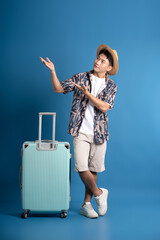 Full body image of Asian guy carrying suitcase travel and posing on blue background