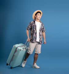 Full body image of Asian guy carrying suitcase travel and posing on blue background