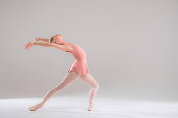 Ballerina in pink leotard dancing on white background.