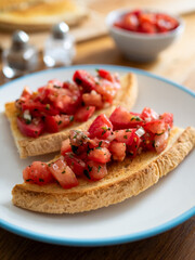 Tasty bruschetta with tomato and onion served on white plate on wooden table
