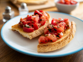 Tasty bruschetta with tomato and onion served on white plate on wooden table
