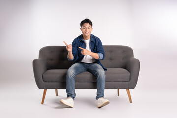 Full body image of young Asian man posing on sofa on white background