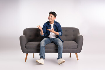 Full body image of young Asian man posing on sofa on white background