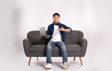Full body image of young Asian man using laptop sitting on sofa on white background