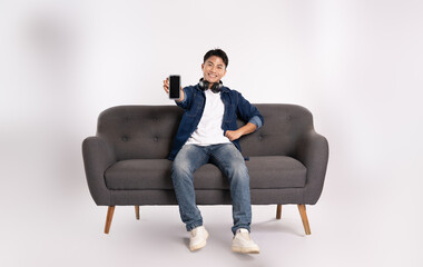 Full body image of young Asian man using phone sitting on sofa on white background