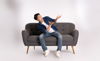 Full body image of young Asian man posing on sofa on white background