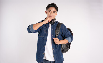 Fototapeta premium Portrait of Asian male student wearing headphones and schoolbag posing on white background