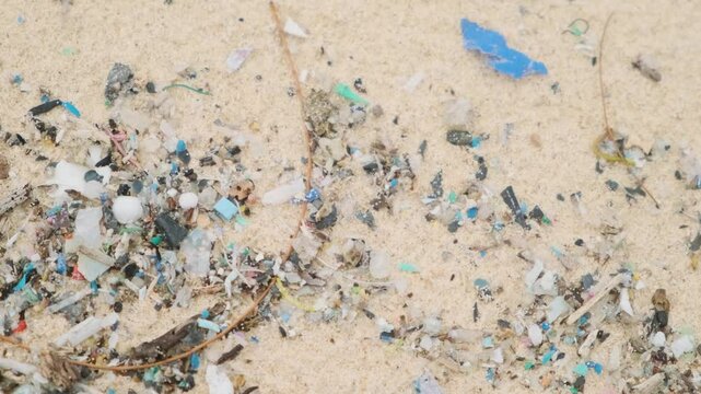Sea shore pollution. Close up of microplastic particles and debris on sandy beach on Phuket island, Thailand. Garbage and trash on the sand. Environmental challenges and marine pollution