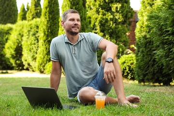 Man with laptop and juice on green lawn outdoors