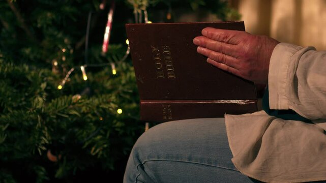 Woman reads Bible by decorated Christmas tree 